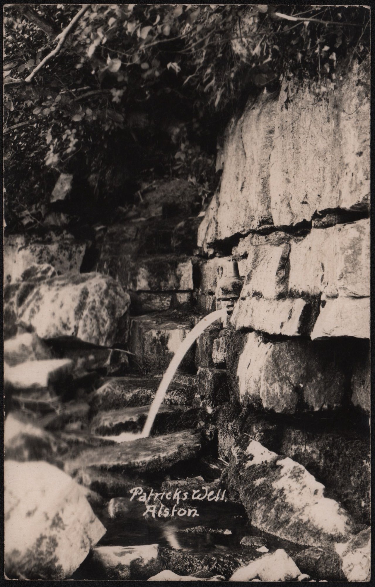 Coll. AMHS. . Below Cats Scaur/Scarr by the banks of the Tyne between The Holmes and Randalholme meadows lies the spring, Patrick's Well. Named after the landlord, Patrick, of the Greyhound Inn in Alston who placed the first iron drinking cup on the chain - not visible on this view.